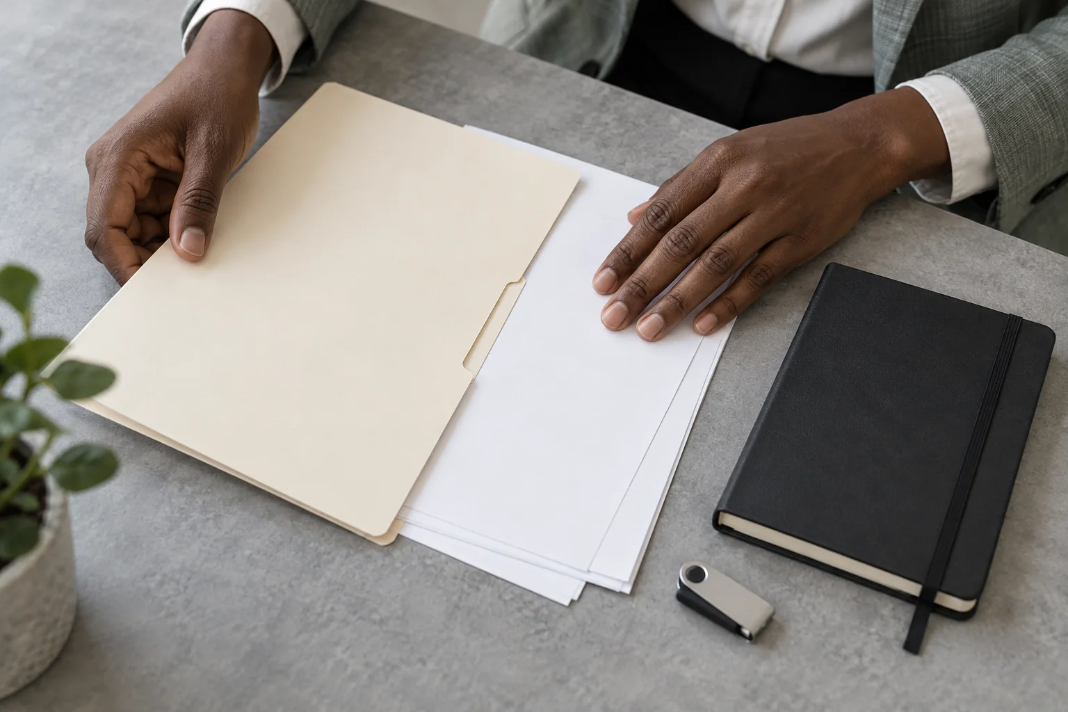 Des mains organisent une chemise, des feuilles et une clé USB sur une table.